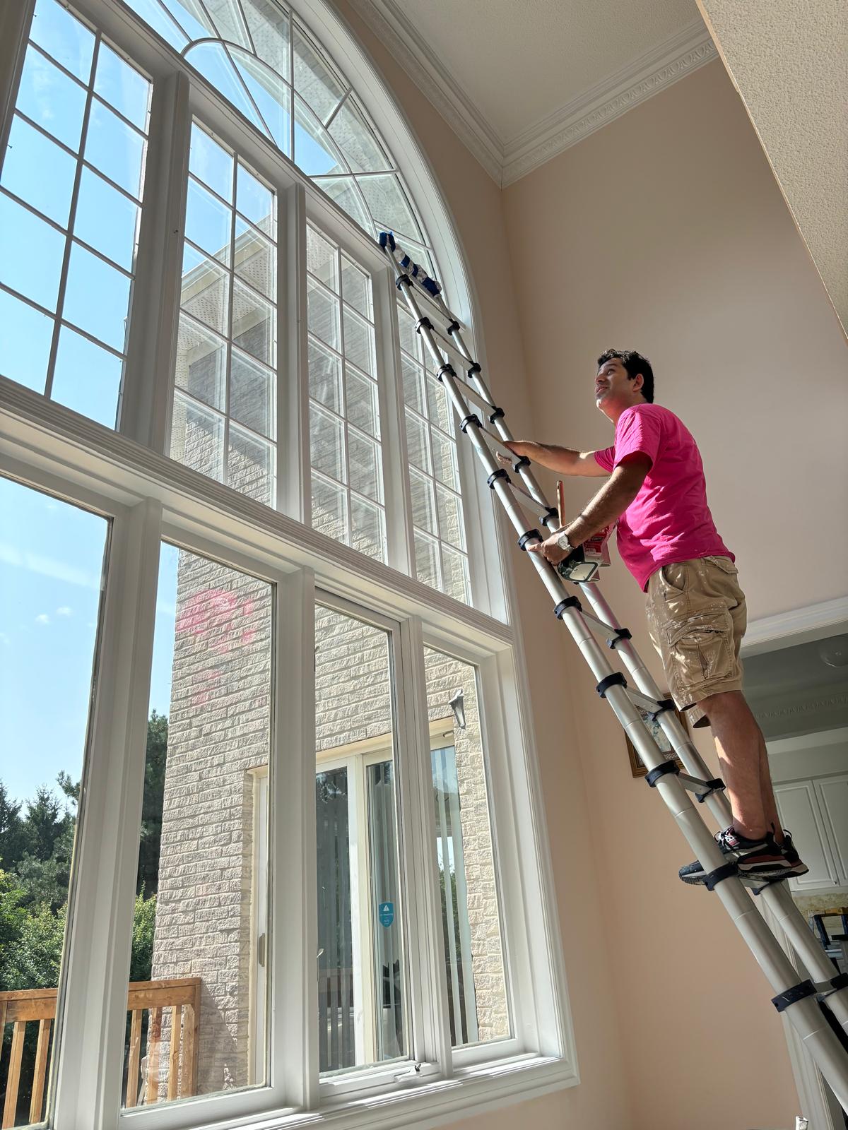 Painter climbing a 21-foot ladder to paint interior window trim in a high-ceiling room. Areas that are difficult to reach, such as stairwells or rooms with intricate architectural details, may require more time and effort, impacting the price per square foot of painting. Cost of Interior House Painting in Toronto 2024.