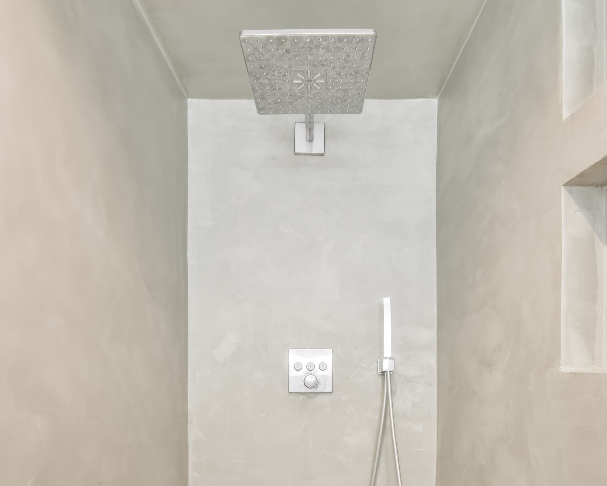 Shower interior featuring walls, floors, and ceiling all finished in a smooth beige microcement for a sleek, modern look in a house in Annex, Toronto.