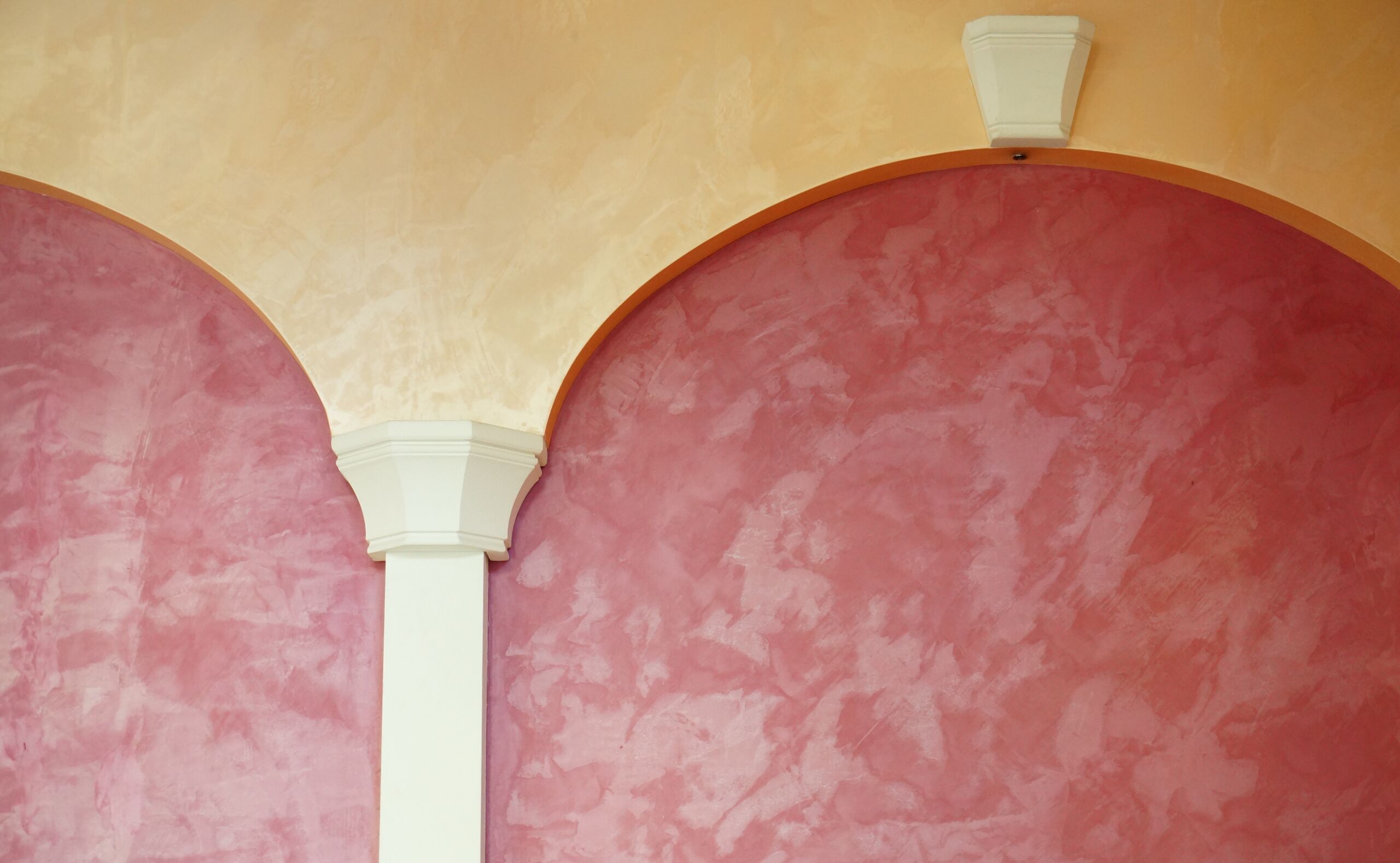 Close-up of a pink Venetian plaster finish wall with an arched design in bone color Venetian plaster finish, exterior.