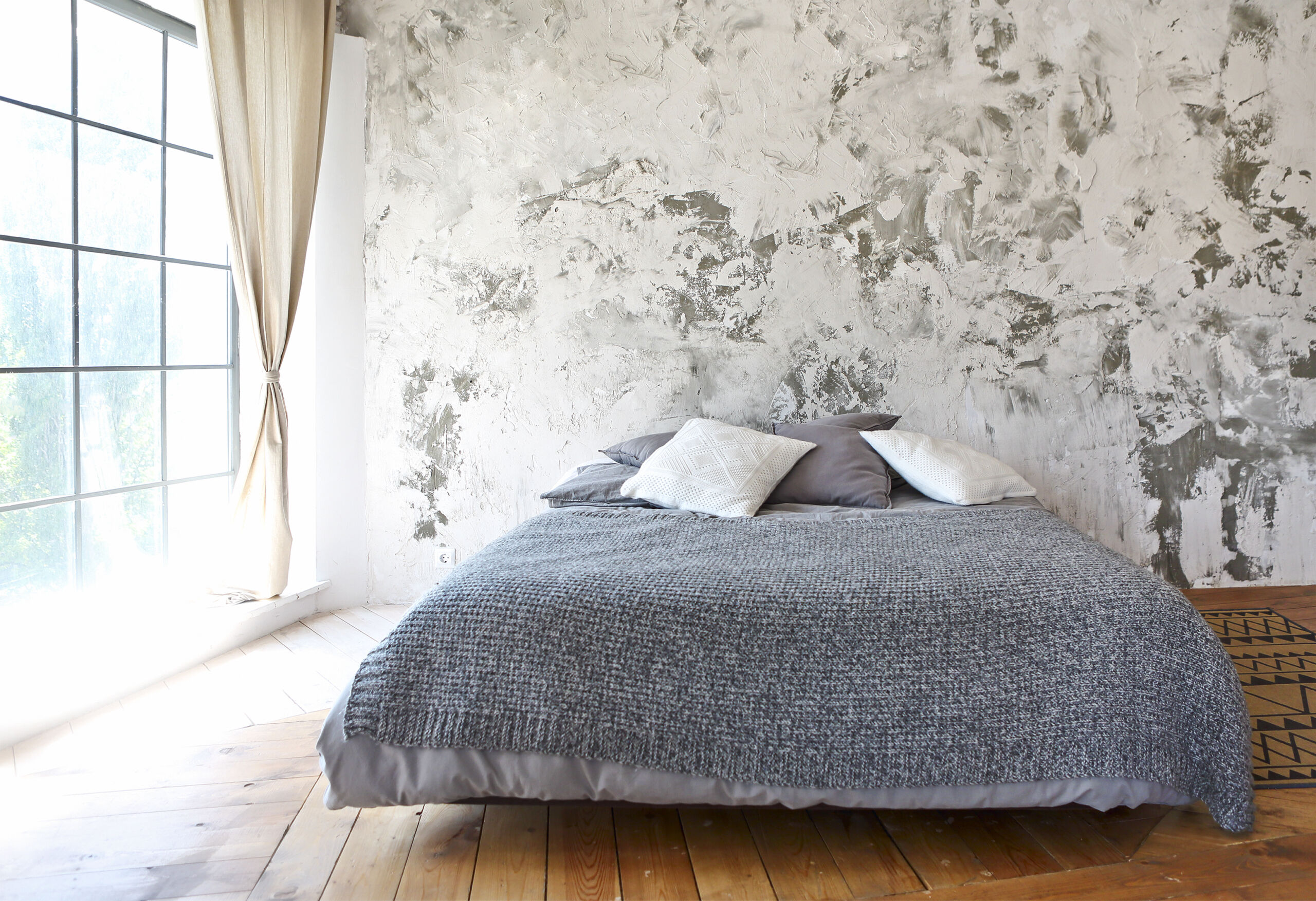 Modern industrial microcement textured wall in a loft bedroom with an off-white and dark gray messy artistic finish.