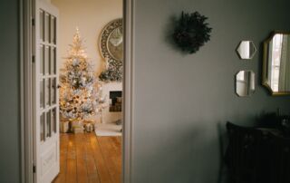 Interior view of a fireplace and Christmas tree from an adjacent room, with a sage green accent wall in the background.