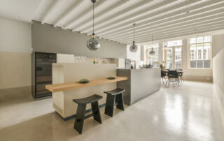 Spacious bright kitchen with a dining area, featuring a microcement range hood and kitchen island in the same microcement texture and colour.